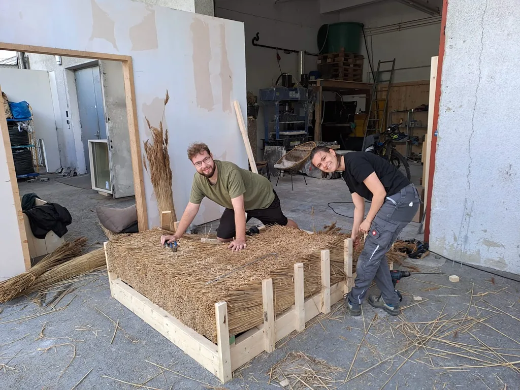 Zwei Personen auf der Arbeit an einem Holzgestellt mit Stroh gefüllt