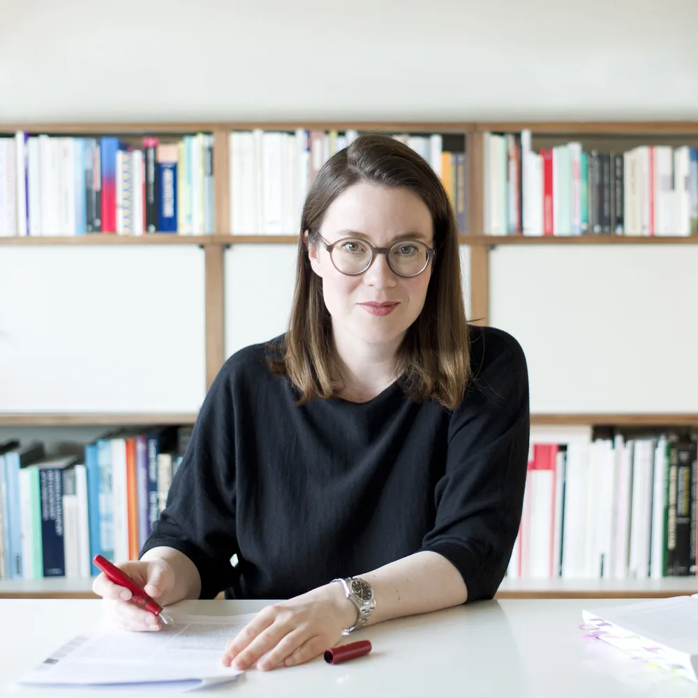 Frida Grahn im Fotoporträt am Schreibtisch sitzend vor einem Bücherregal