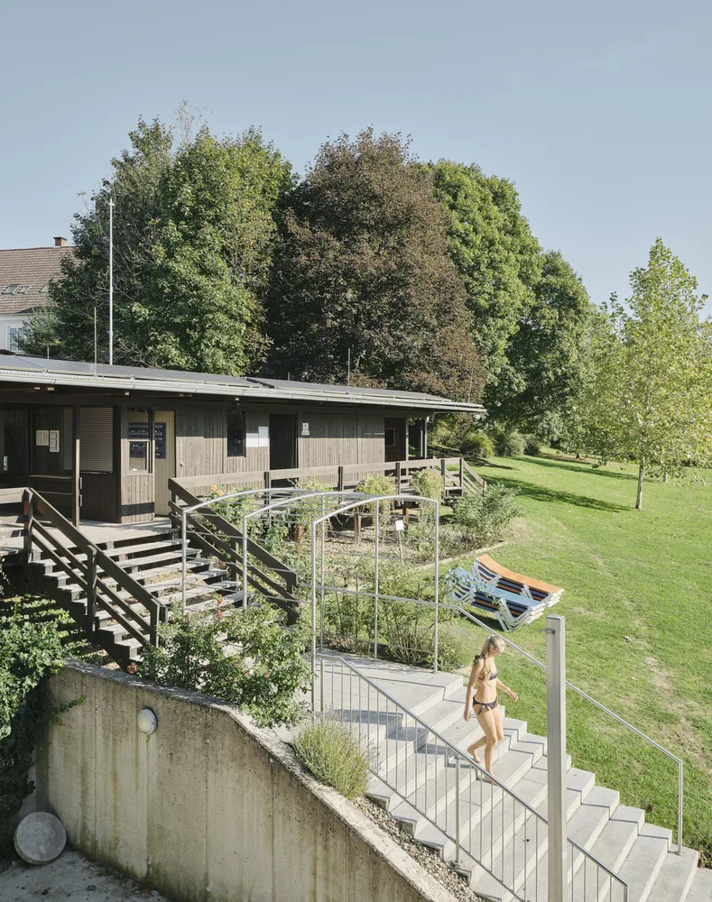 Bild einer Treppe mit einer Person im Badeanzug, im Hintergrund eine Wiese und ein Gebäude aus Holz