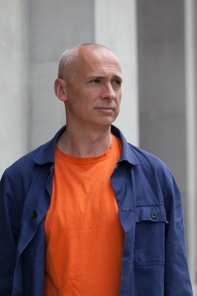 Portrait eines Mannes in einem orangen T-Shirt und darüber ein offenes blaues Hemd