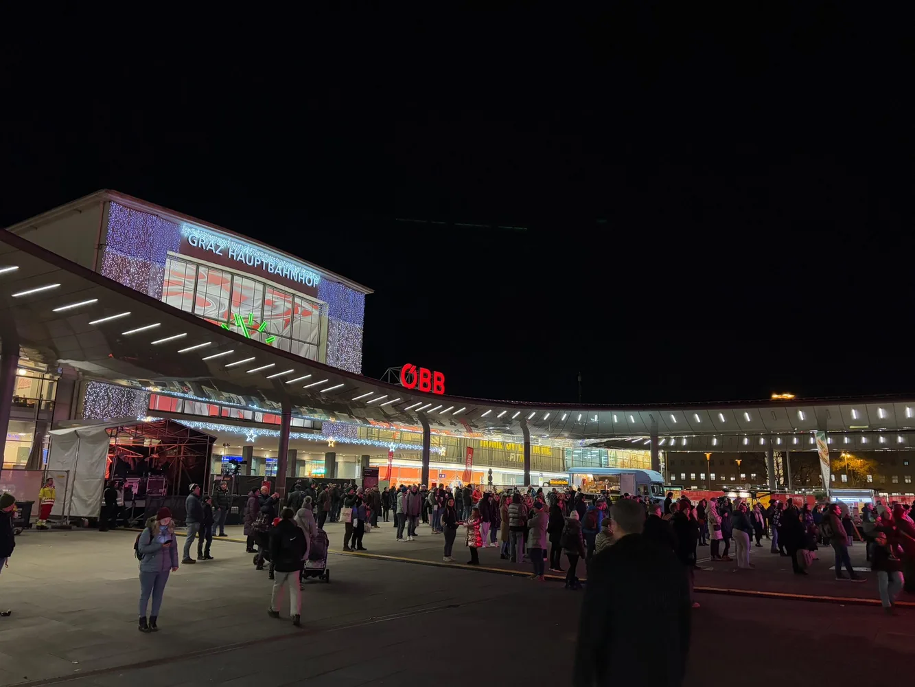 Ansicht eines Platzes bei Nachtlicht, viele Menschen am Platz verteilt