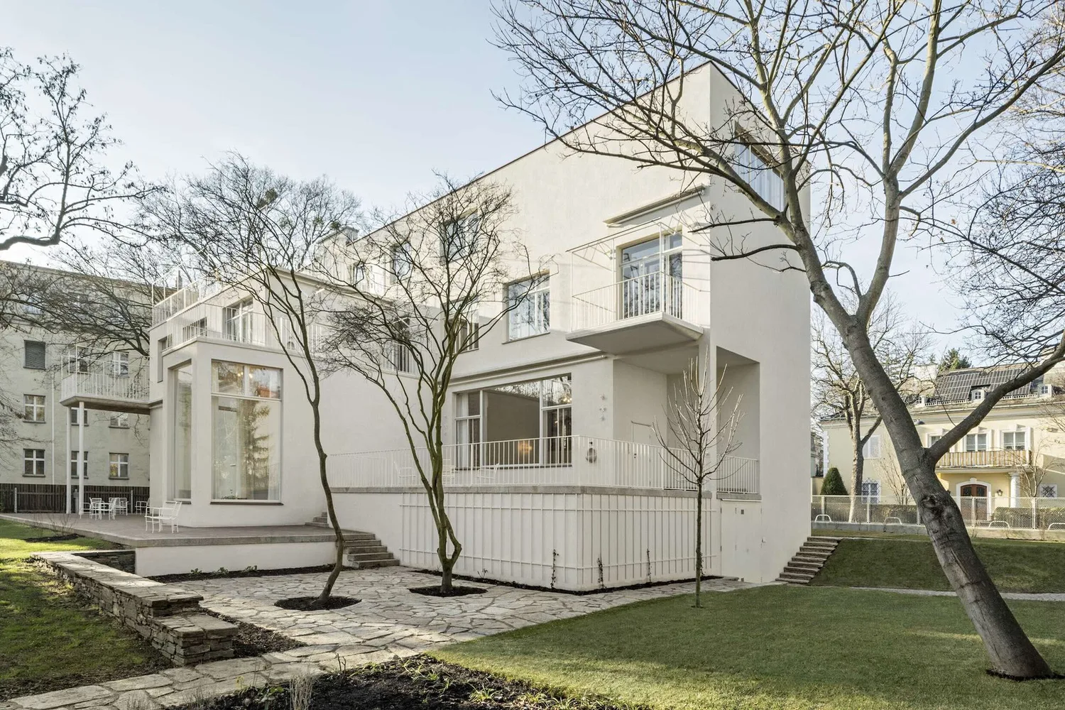 Photo der Fassade einer mehrgeschossigen weißen Villa, umgeben von einem großen Garten
