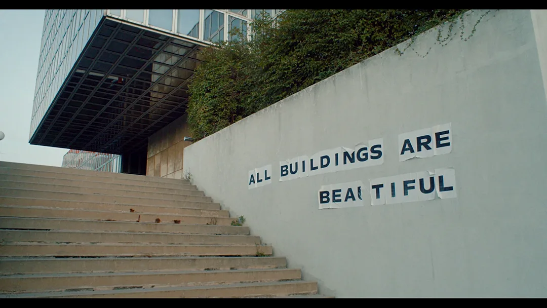 Treppenaufgang mit Slogan, Filmstill aus All Buildings Are Beautiful, Christoph Schwarz, 2026