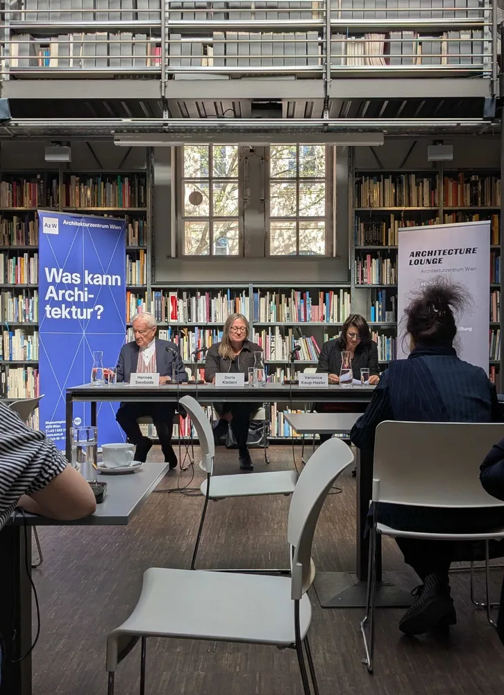 Drei Personen sitzen hinter einem Tisch, hinter ihnen ein Bücherregal