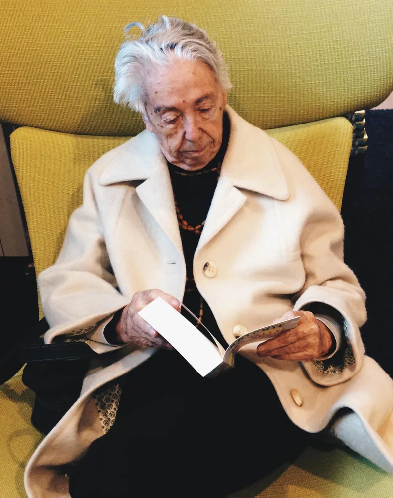 Foto einer Frau mit einem Buch in der Hand, auf einem gelben Ohrensessel sitzend