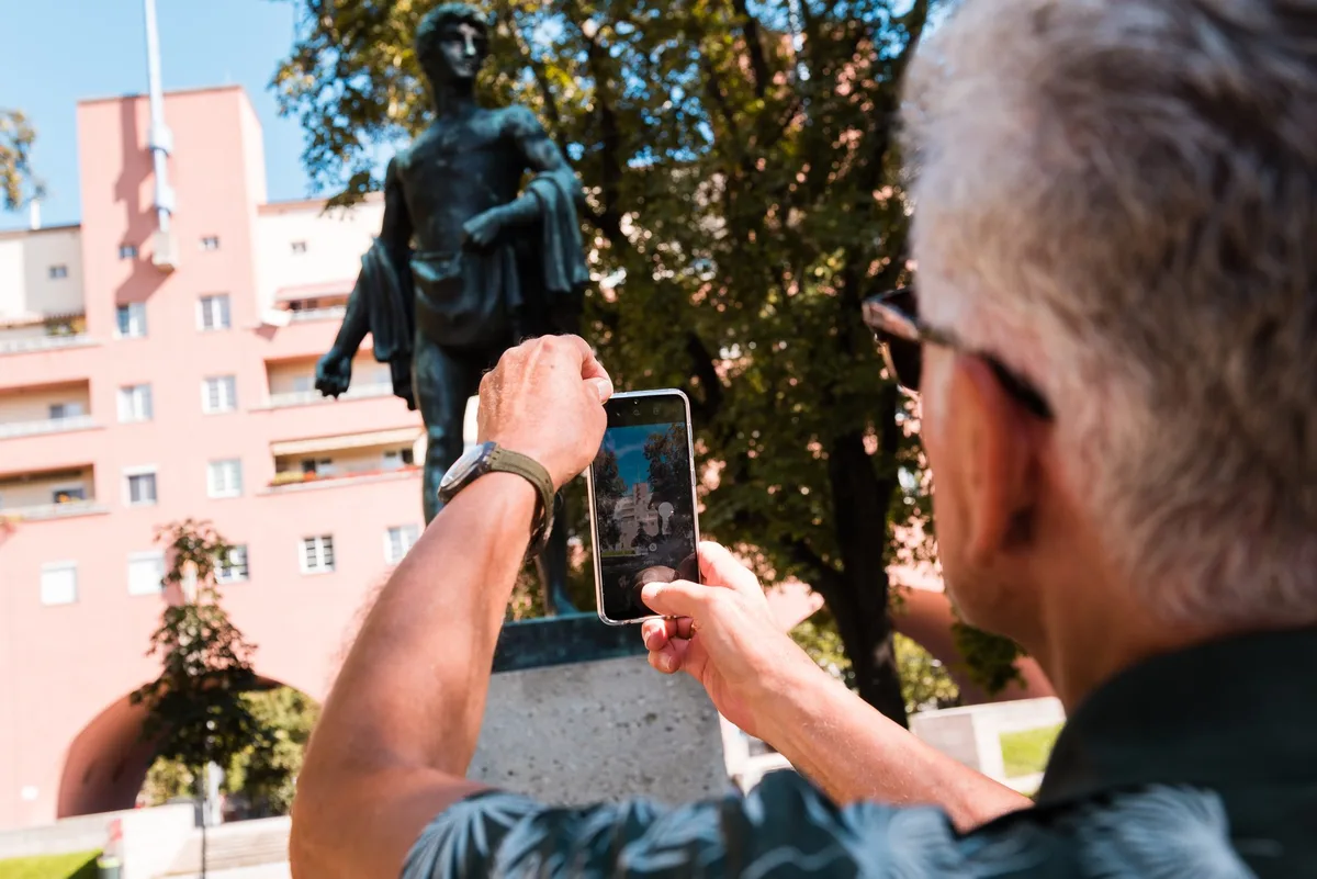 Man mit Handy vor rosa Gebäude, Stadtspaziergänge Rotes Wien im Waschsalon, 2024, © Stefan Zamisch