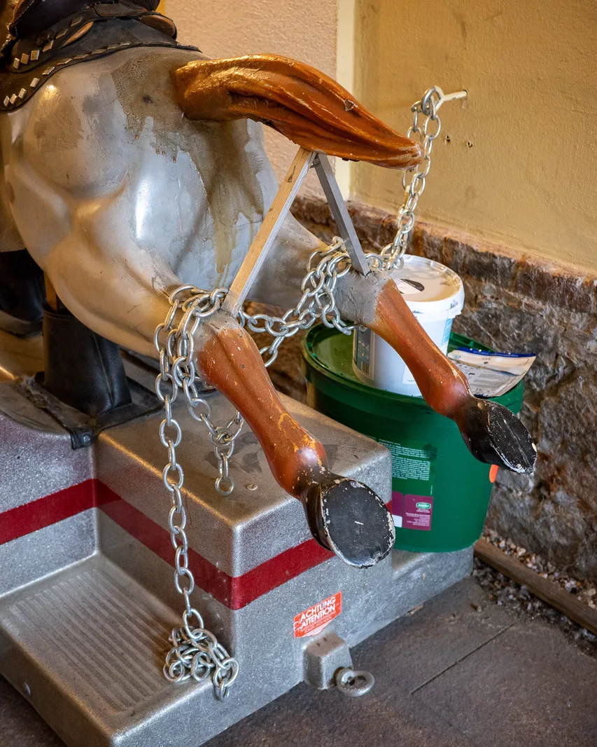 Kinder-Fahrautomat in Form eines Huftieres, in Ketten eingebunden, von hinten fotografiert