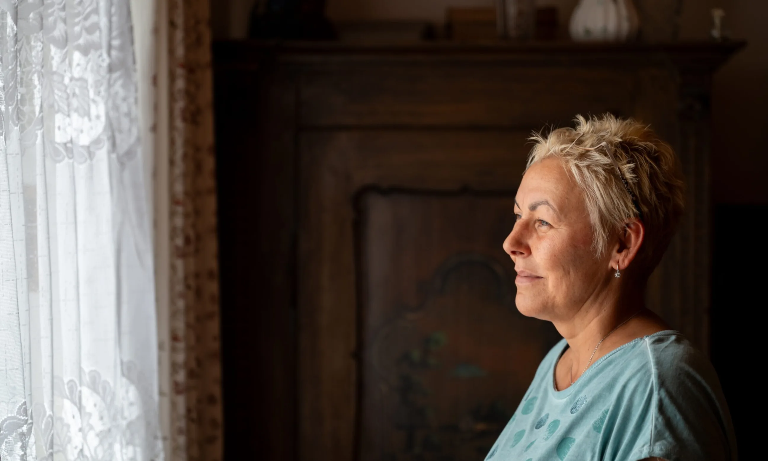 Frau blickt durch den Vorhang aus dem Fenster raus