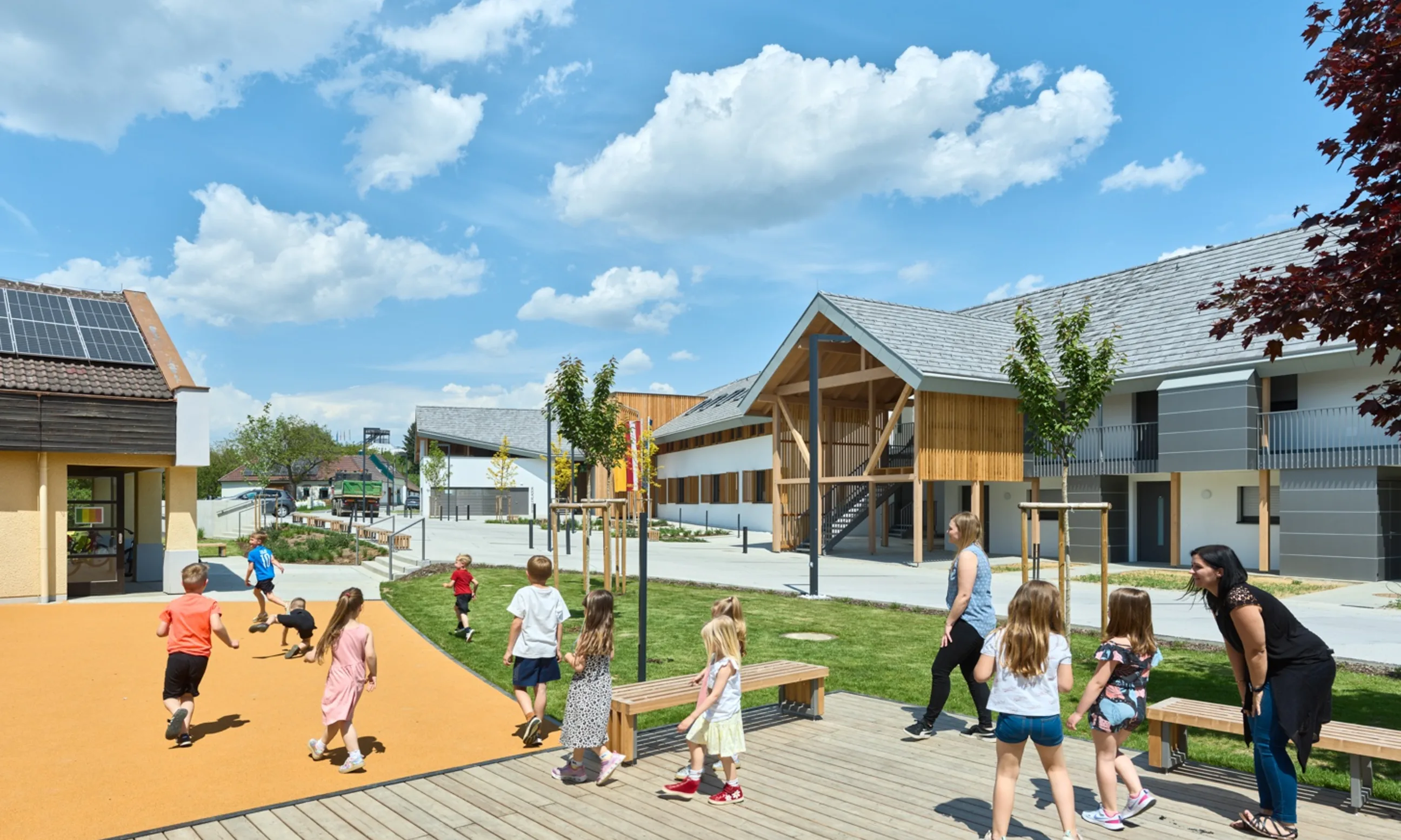 Spielende Kinder im Park. Im Hintergrund zwei Gebäude aus Holz
