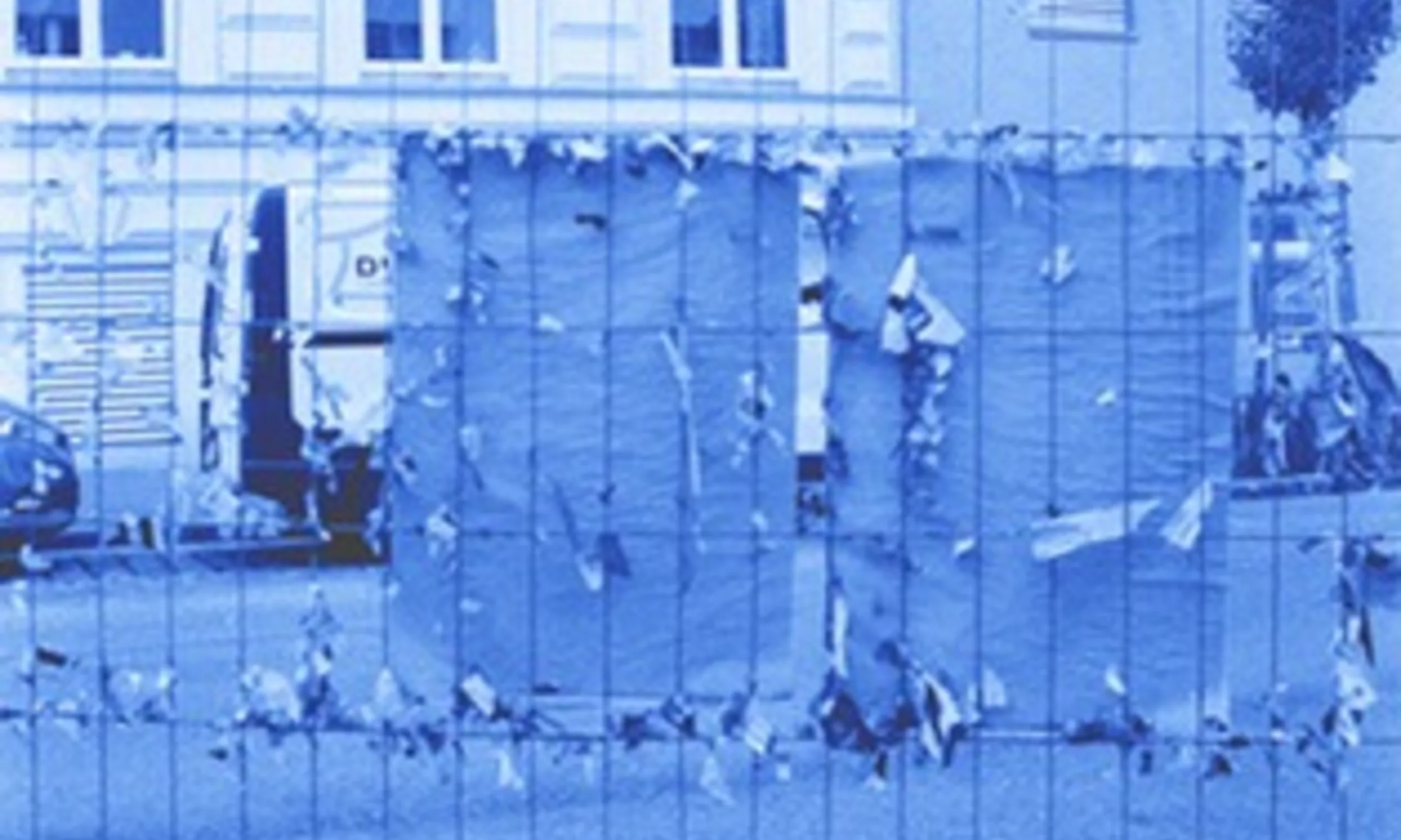 Straßenraum, im Vordergrund ein Baugerüst mit zerrissenen Plakaten