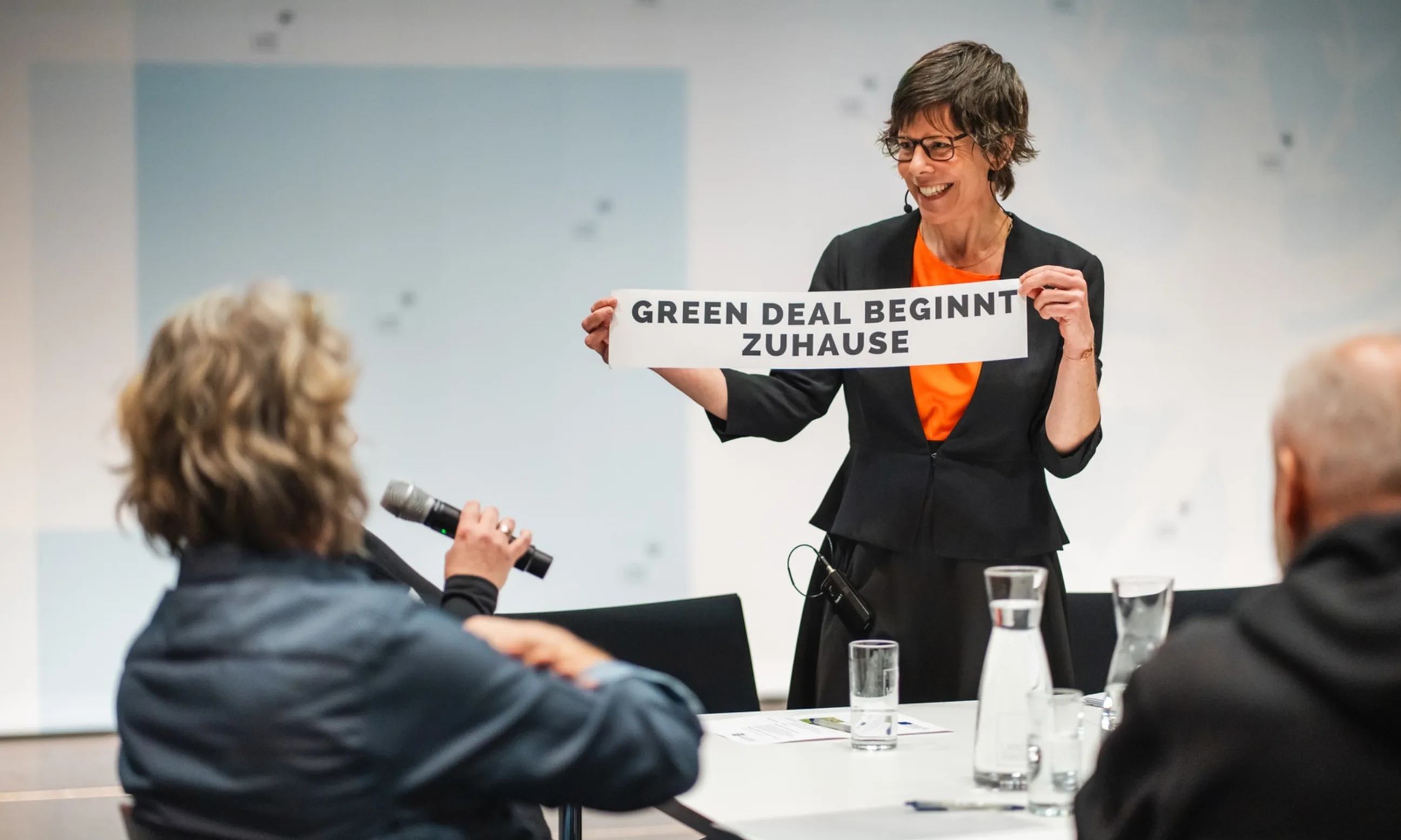 Frau hält ein Transparent mit der Aufschrift "Green Deal beginnt Zuhause"