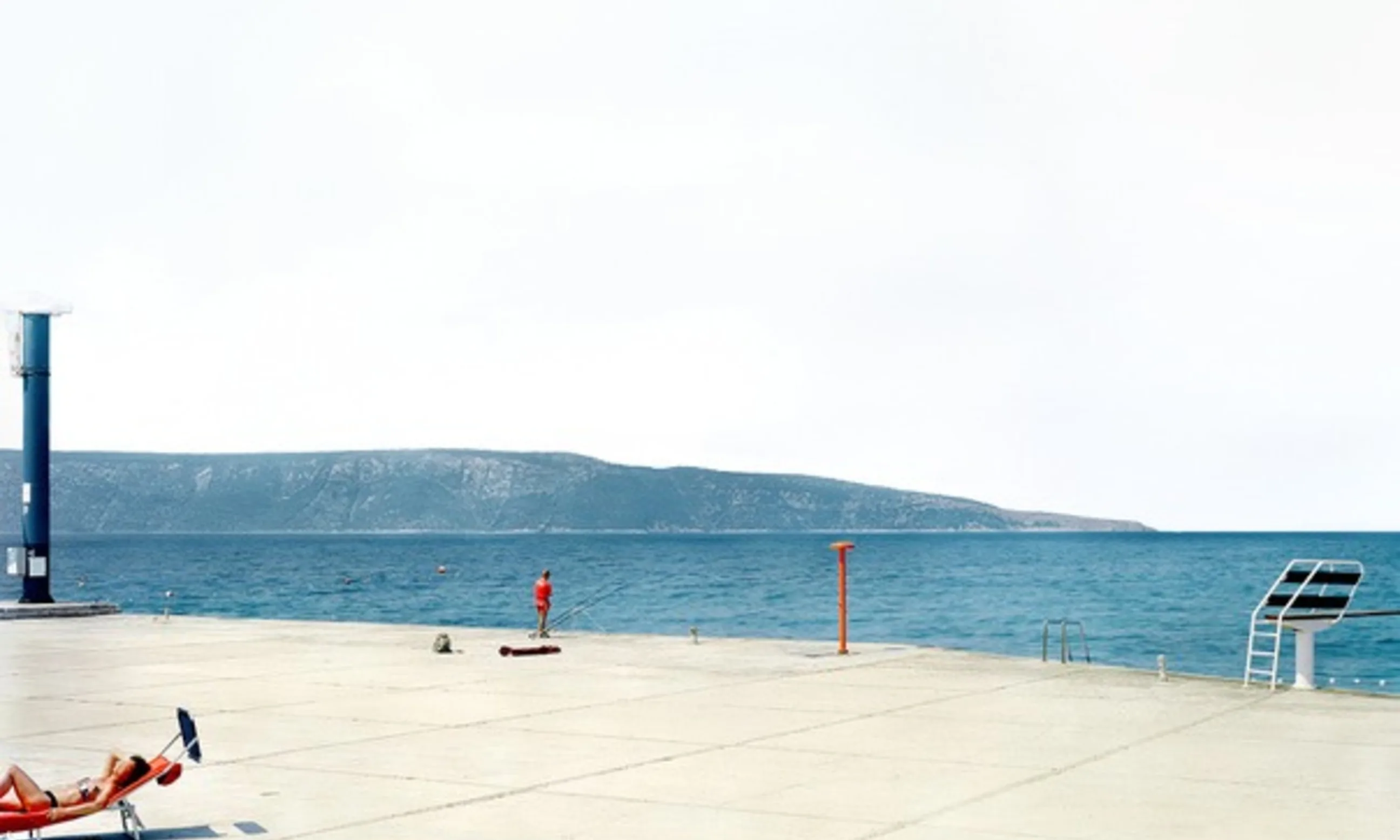 Betonsteg mit zwei Menschen, im Hintergrund das Meer