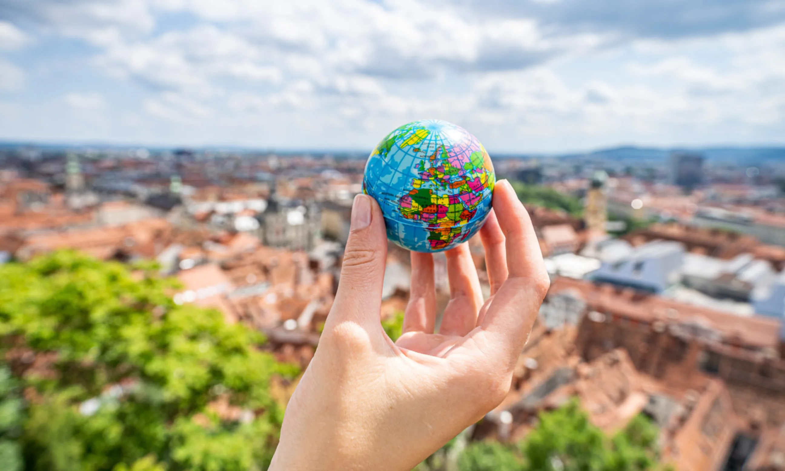 Hand hält kleinen Globus, im Hintergrund die Grazer Dachlandschaft