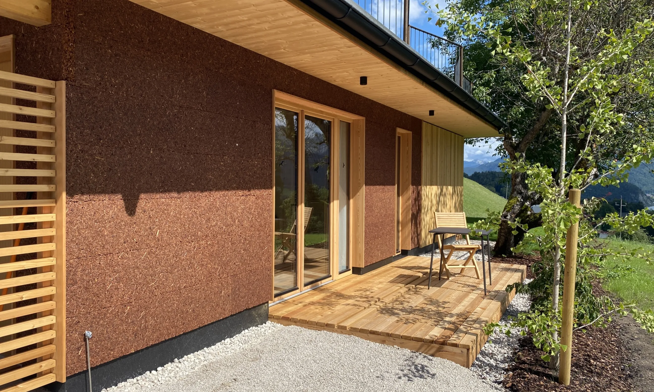 Braunes Gebäude, im Vordergrund Terasse aus Holz, im Hintergrund eine Wiese