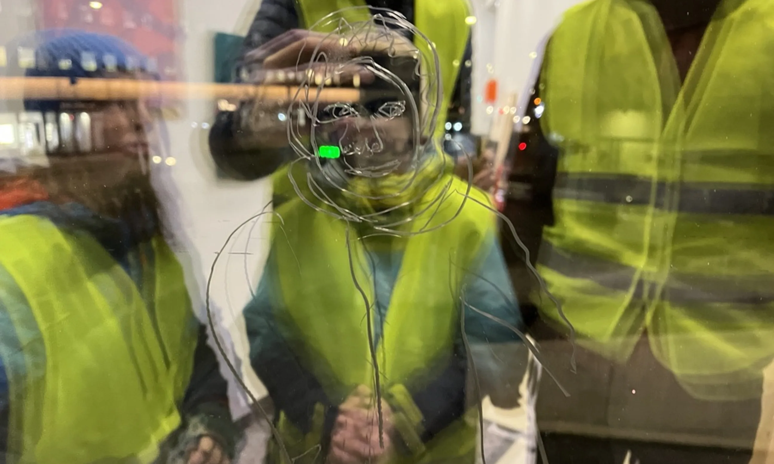 Spiegelung in einer Glasscheibe mehrerer in gelbe Warnwesten angezogener Menschen