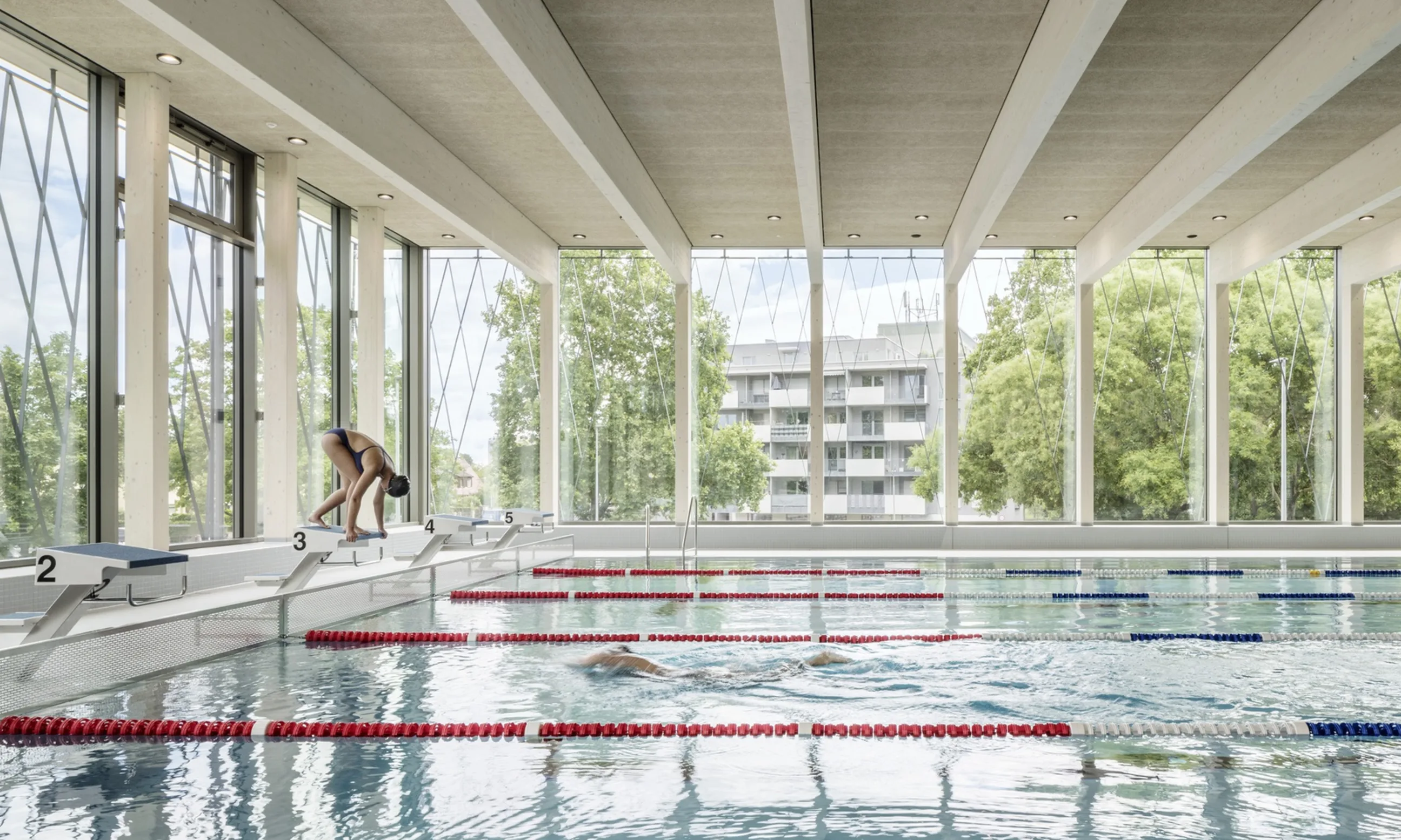 Schwimmhalle mit Holzoberflächen, im Vordergrund das Schwimmbecken mit zwei schwimmenden Personen