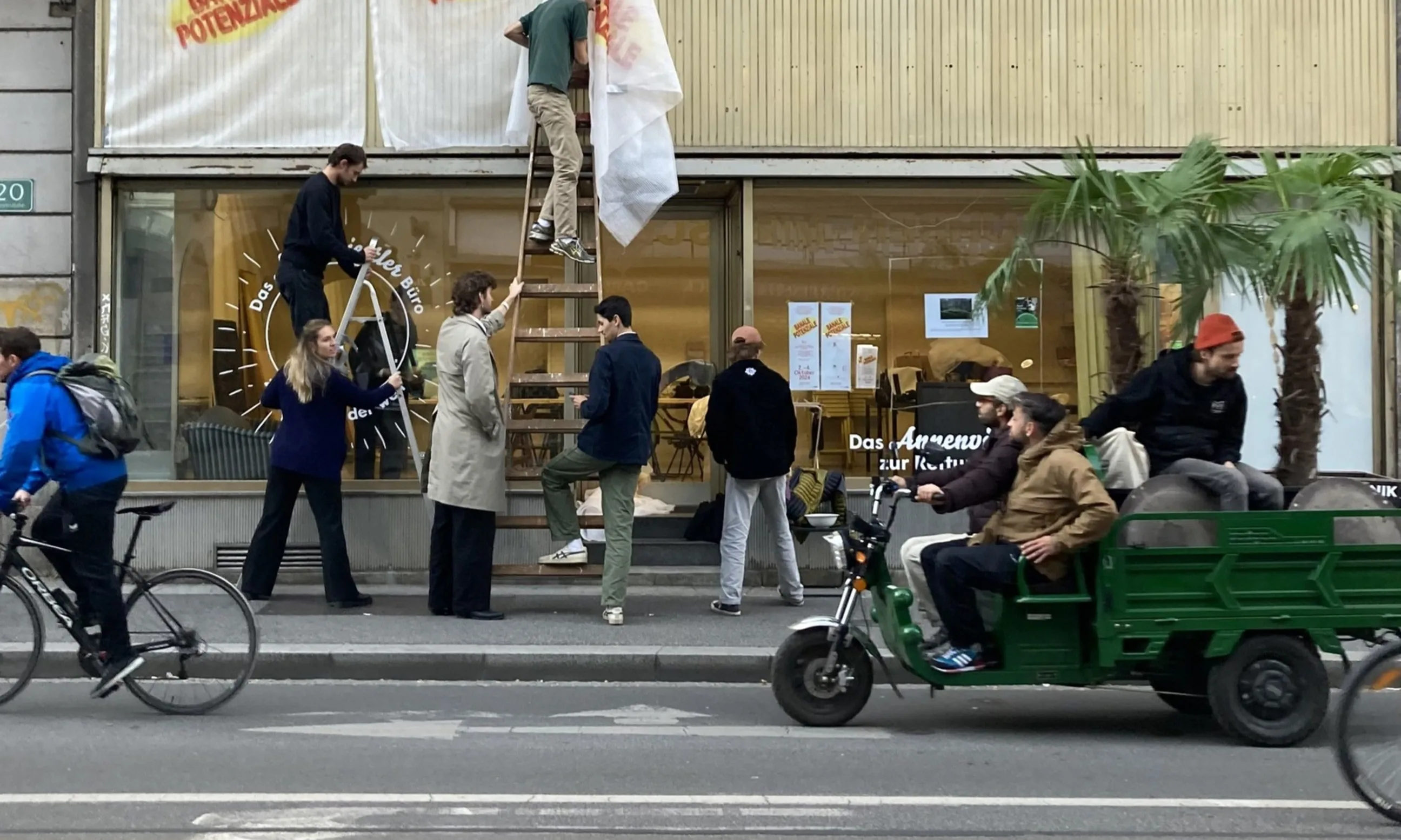 Straßenraum mit Menschen, auf einer Vitrine wird die Aufschrift banale potenziale angebracht