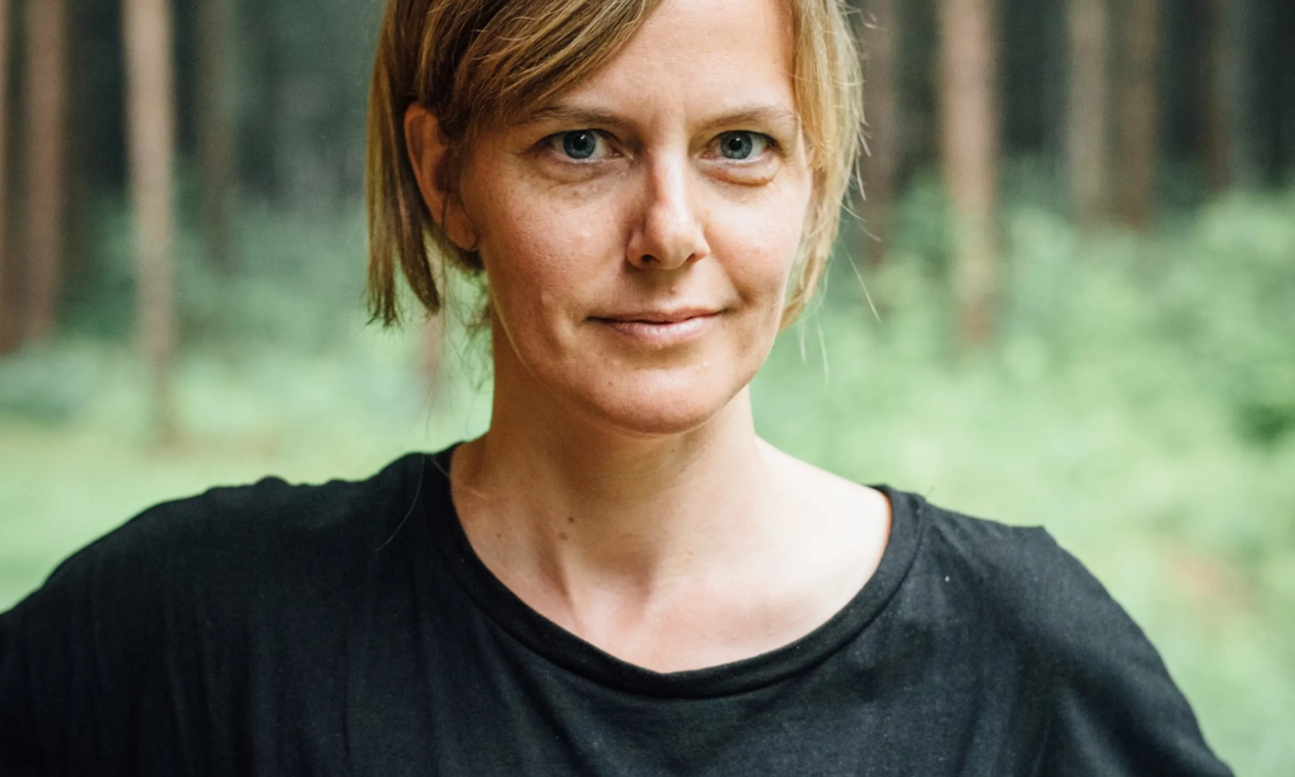 Portrait einer Person in schwarzem Tshirt, im Hintergrund eine Waldlandschaft