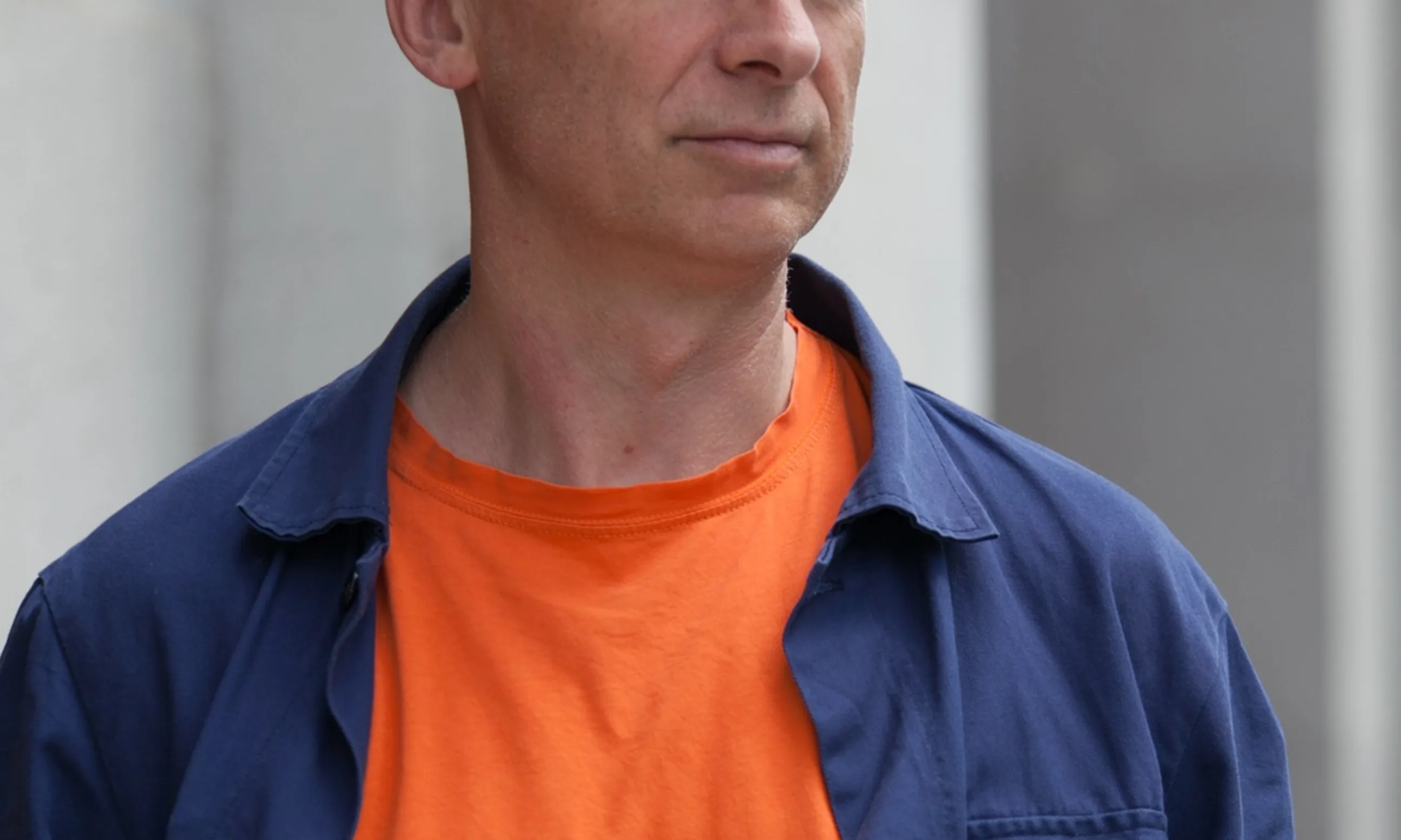 Portrait eines Mannes in einem orangen T-Shirt und darüber ein offenes blaues Hemd