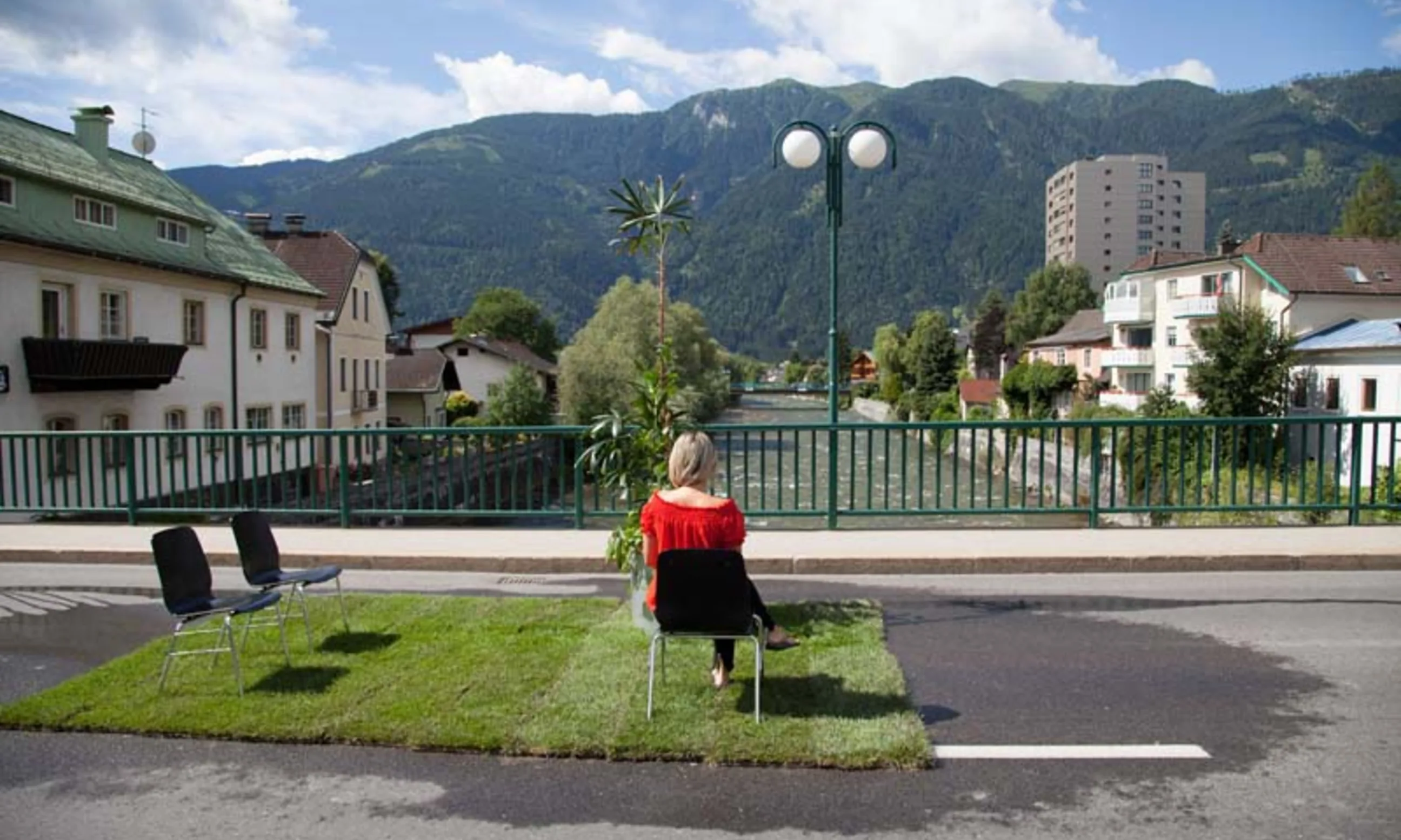 Eine Frau sitzt mit dem Rücken gewandt zur Kamera auf einer Flussbrücke, links und rechts von ihr lokale Architektur