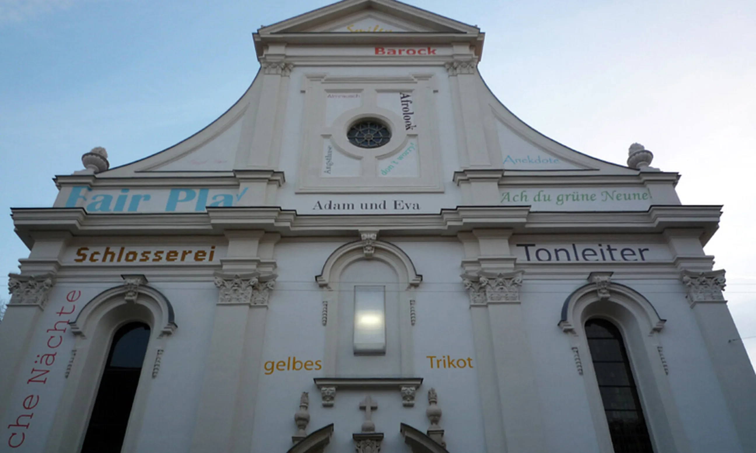 Photo der Fasade einer barocken Kirche mit bunten Aufschriften