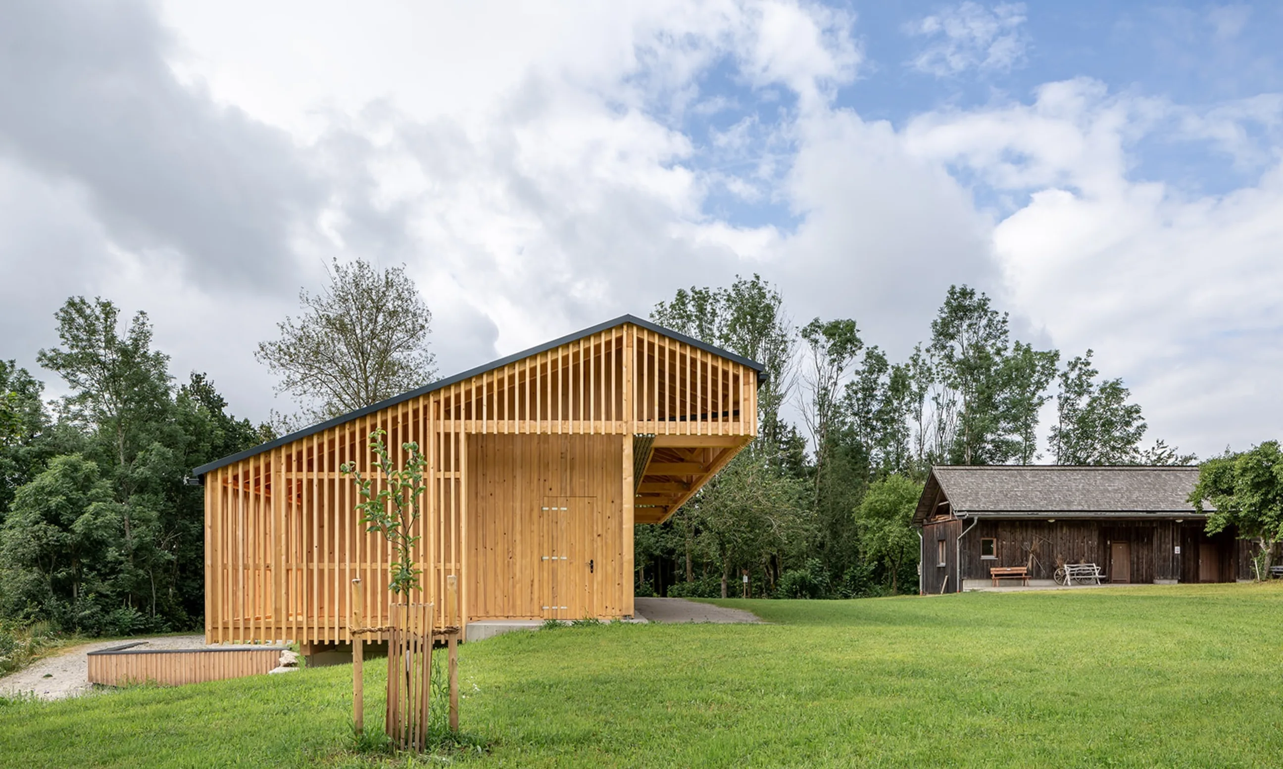 Eingeschoßiges Gebäude aus Holz, im Hintergrund ein Wald