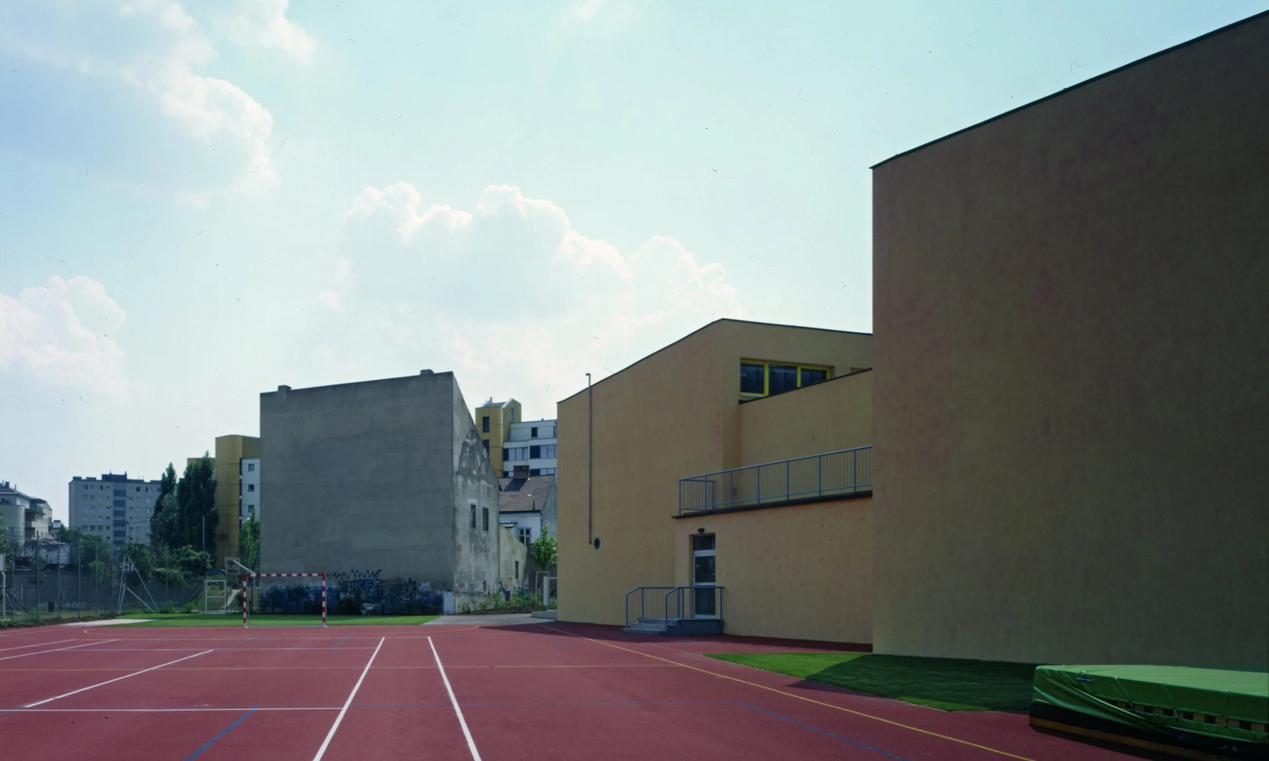 Bild eines Sportfeldes, im Hintergrund ein gelbes und ein graues Schulgebäude