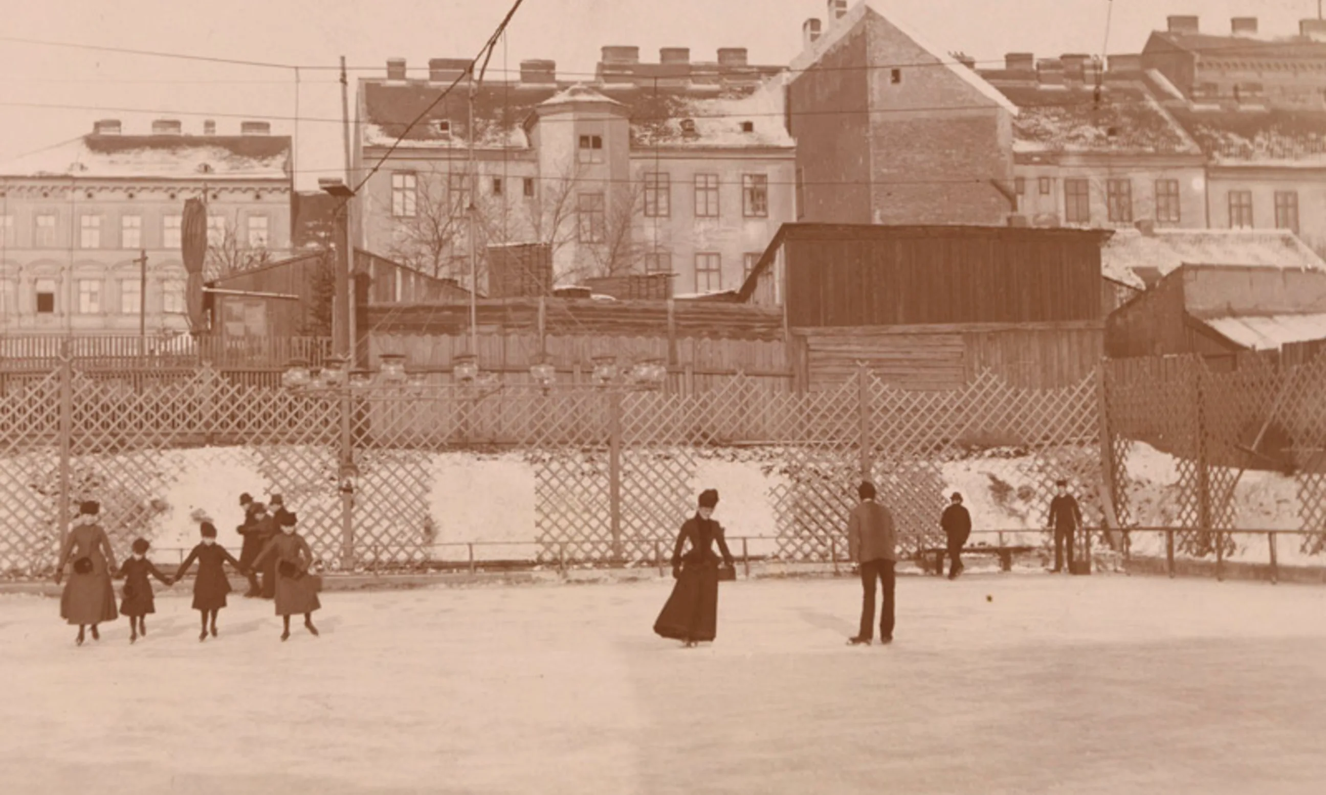 Photo einer Eisfläche mit Menschen darauf verteilt, im Hintergrund Gebäudefassaden