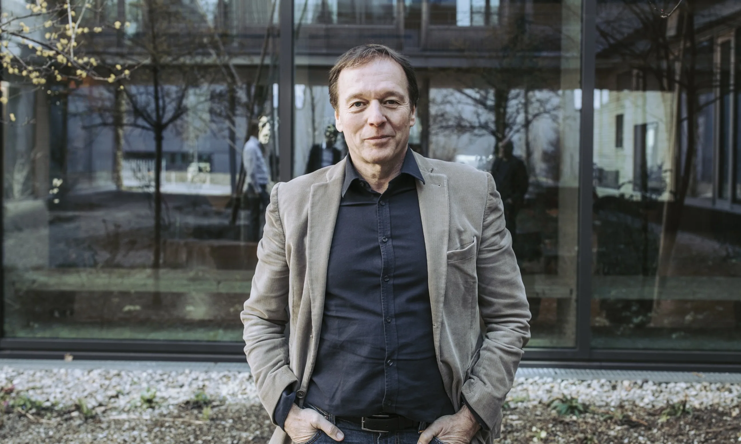 Porträt eines Mannes in Jeans und Sakko, im Hintergrund eine Glasfassade