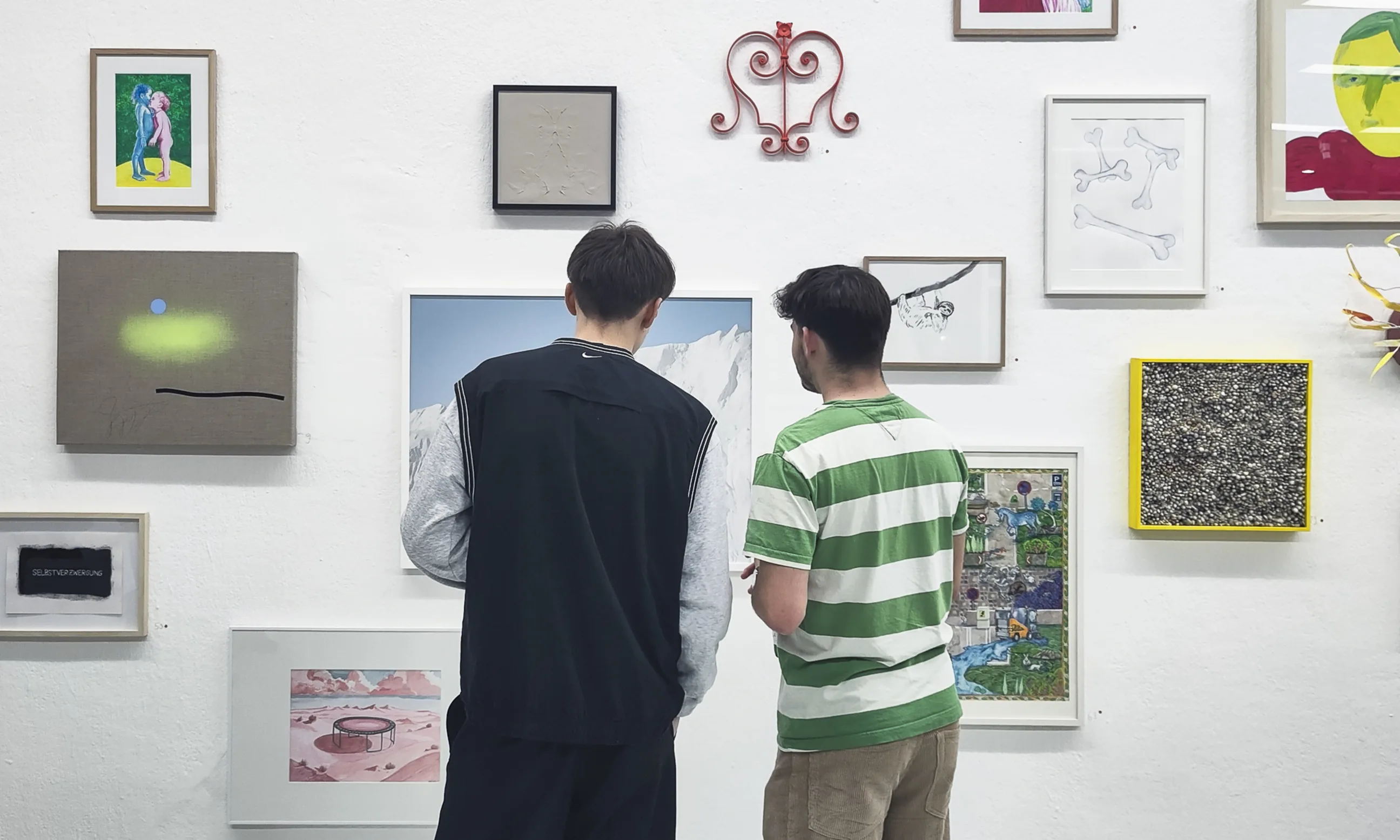 Zwei Personen, mit dem Rücken zur Kamera gewandt, stehen vor einer Wand mit vielen Kunstwerken