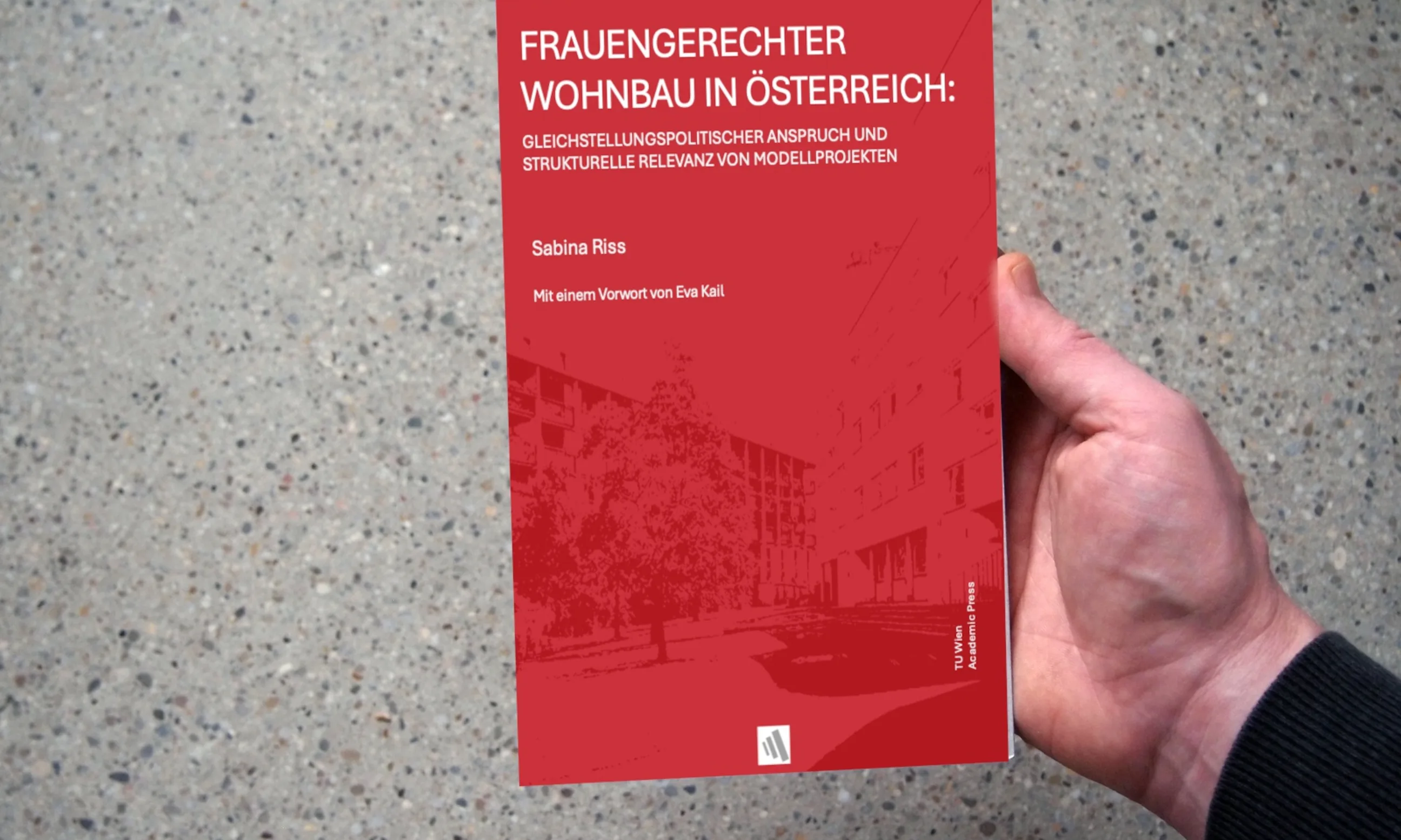 Eine Hand hält ein rotes Buch in der Hand, im hintergrund eine graue Oberfläche