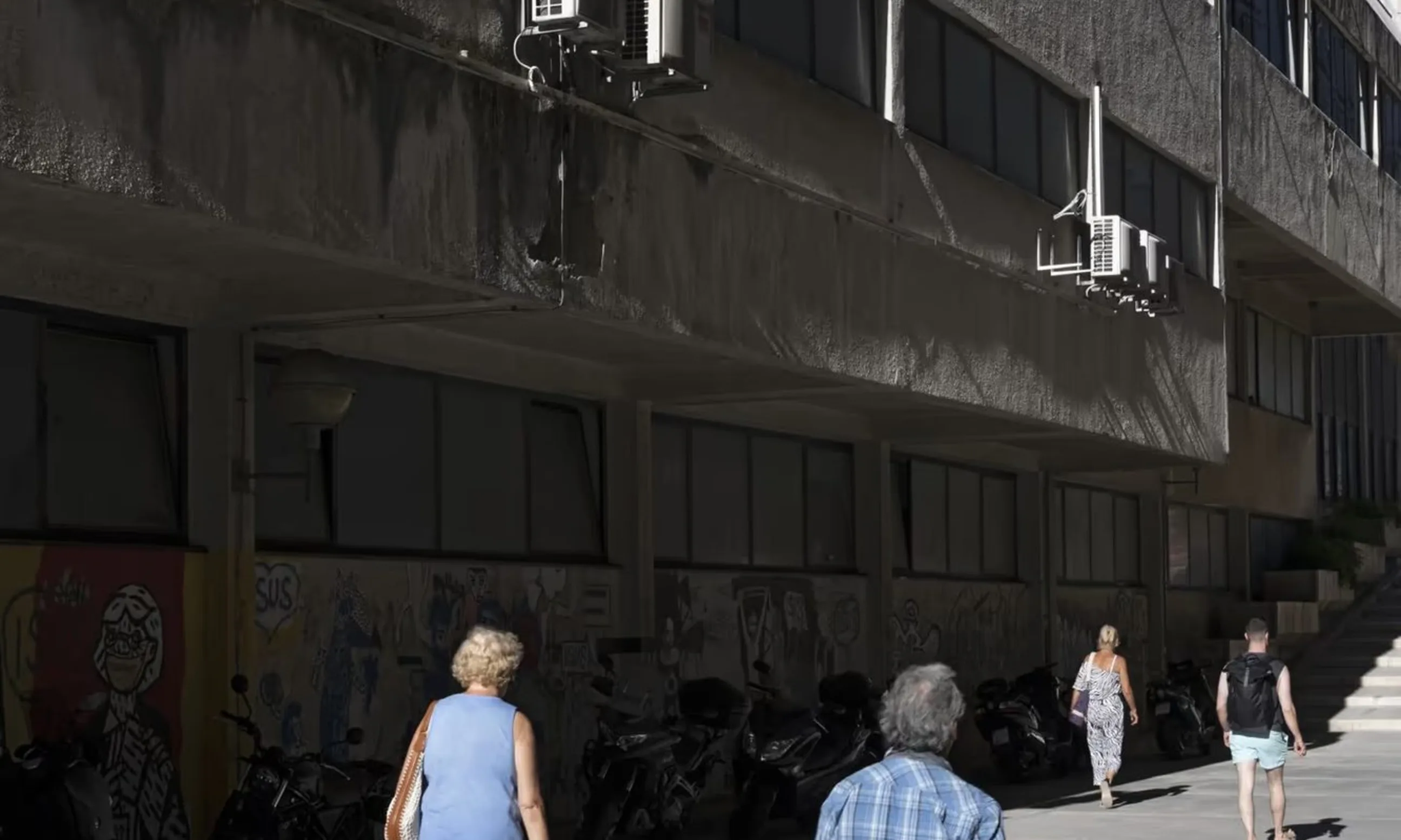 Photo einer Straßenszene, Menschen spazieren an einer Promenade entlang eines Gebäudes