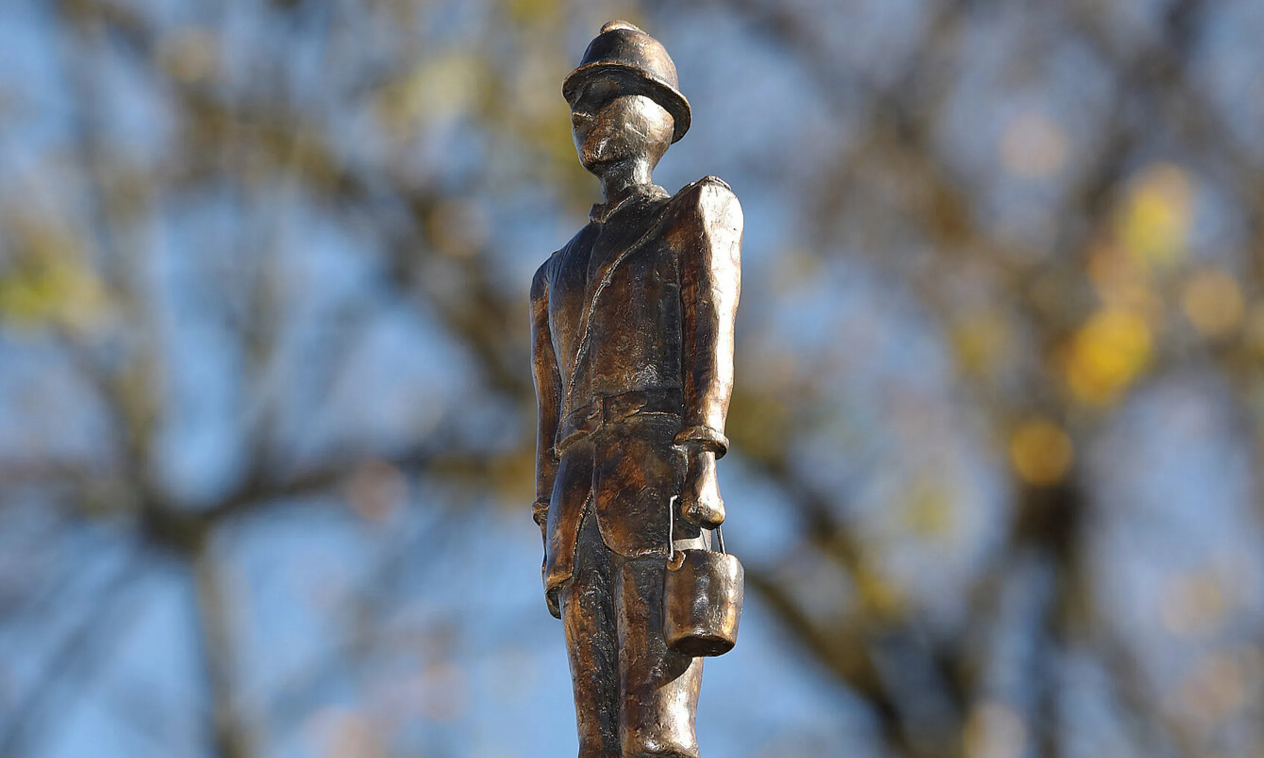 Bronzemännchen eines Feuerwehrmannes in Uniform, im Hintergrund Baumäste und blauer Himmel