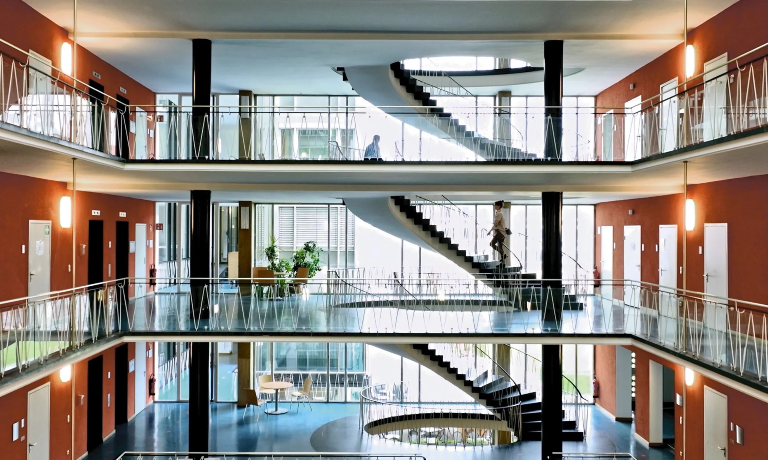 Ein mehrgeschossiges Atrium, links und rechts Balustraden, in der Mitte eine geschwungene Treppe