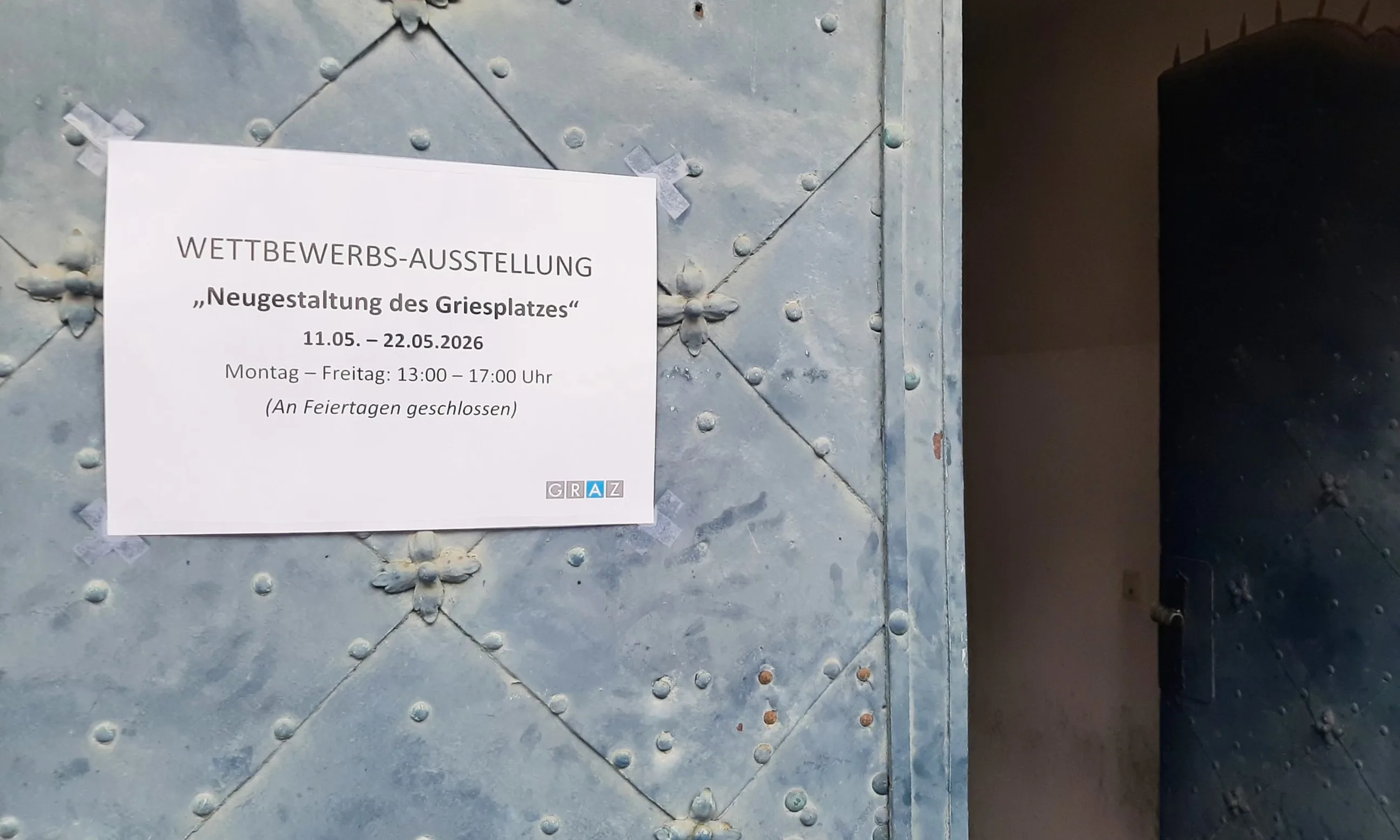 Hinweis zur Ausstellung auf einem grünen Tor aufgeklebt