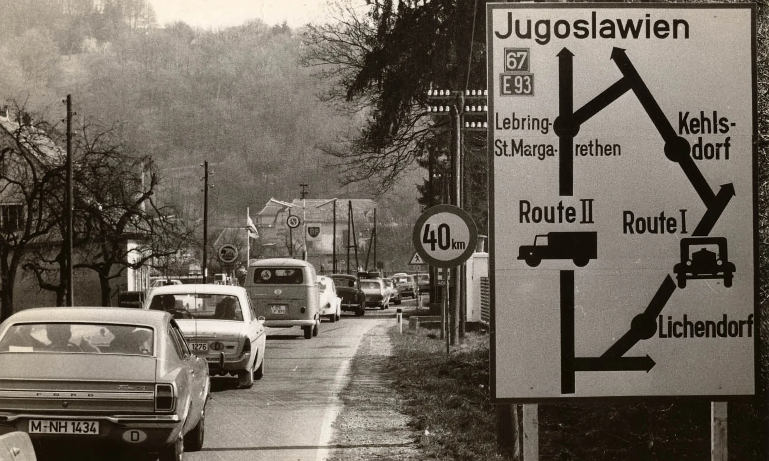 Eine Schlange an Autos fährt eine Straße entlang, rechts im Bild ein Verkehrsschild sichtbar