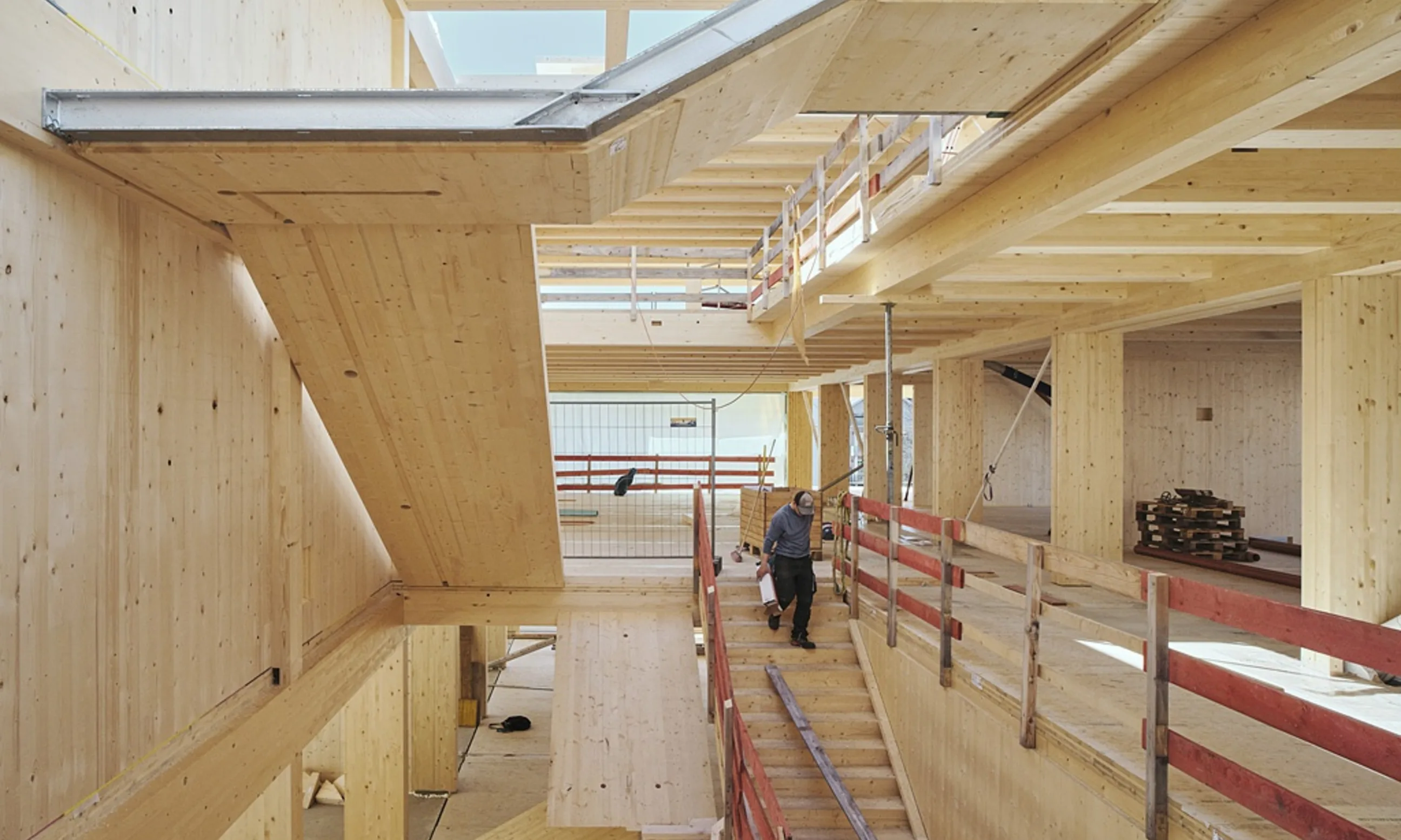 Photo eines Atriums eines mehrgeschossigen Gebäudes aus Holz, ein Arbeiter geht gerade die Stiege runter