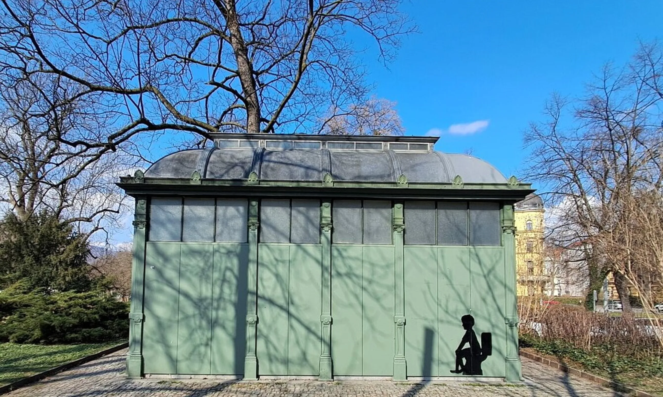 Photo eines grünen WC-Häuschens mit einem schwarzen Aufkleber an der Fassade