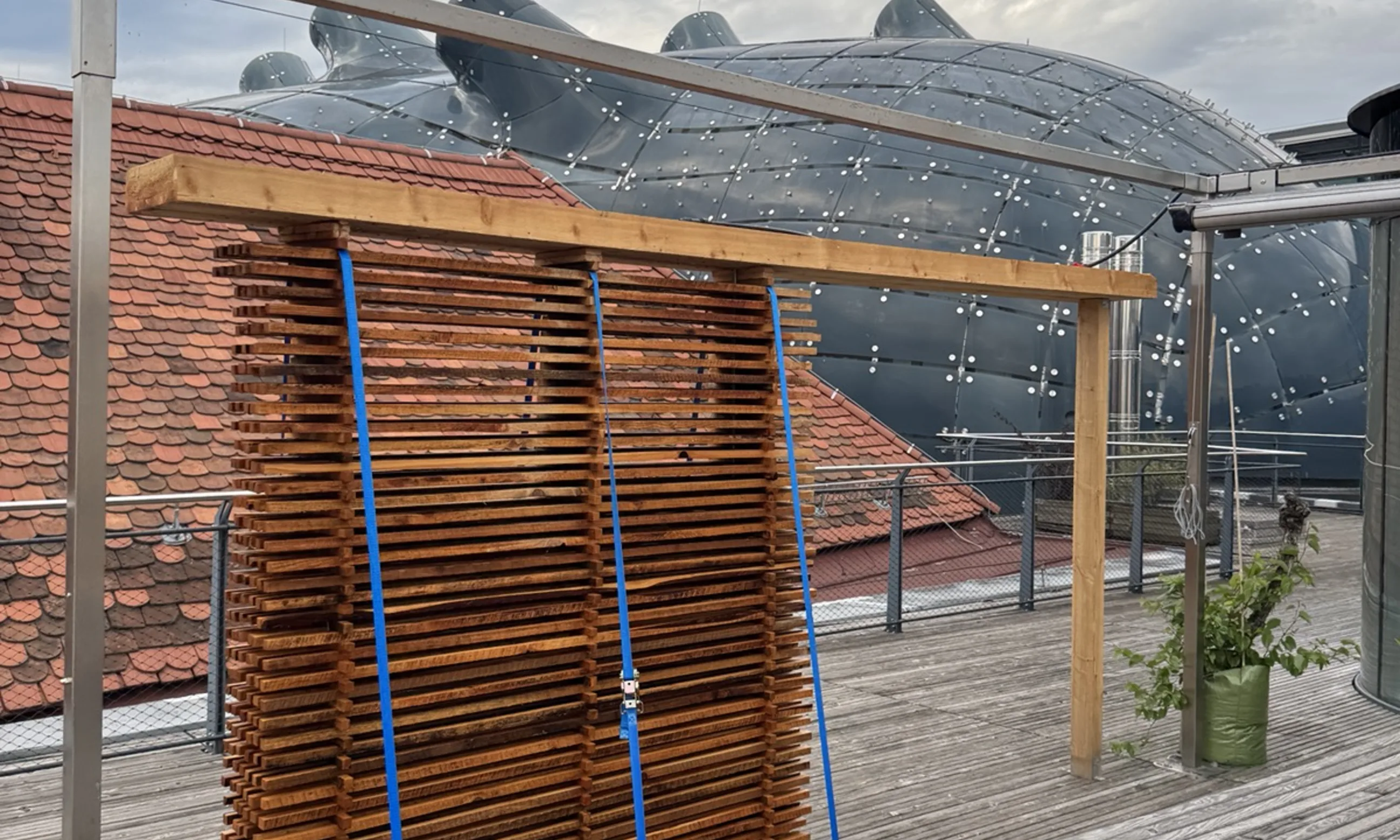 Photo einer Installation aus Holz auf einer Dachterrasse, dahinter das Kunsthaus Graz